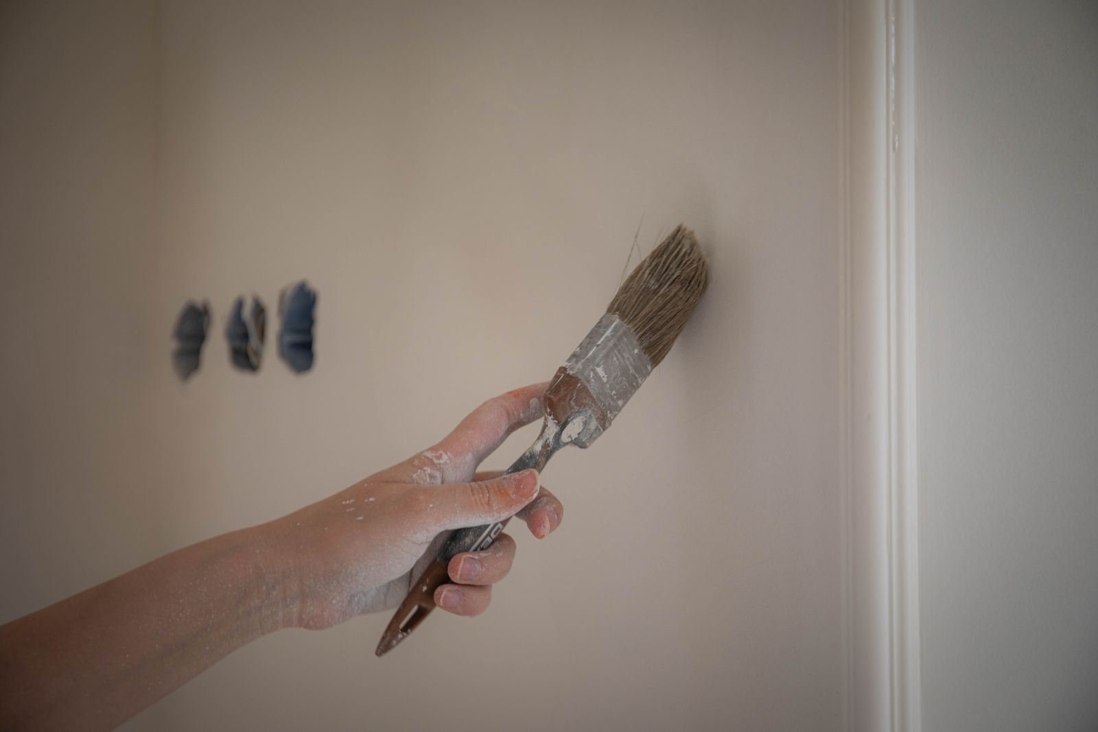 Hand mit einem Pinsel beim Streichen einer hellen Wand neben einer Kante