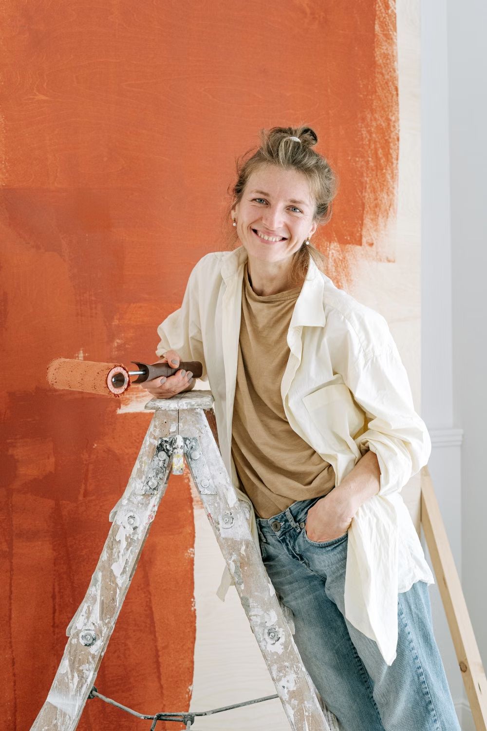 Stockfoto: Frau mit Farbrolle vor einer frisch gestrichenen Wand